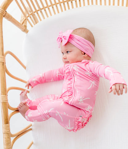 Baby in pink outfit lying on a white blanket with a wicker bassinet.
