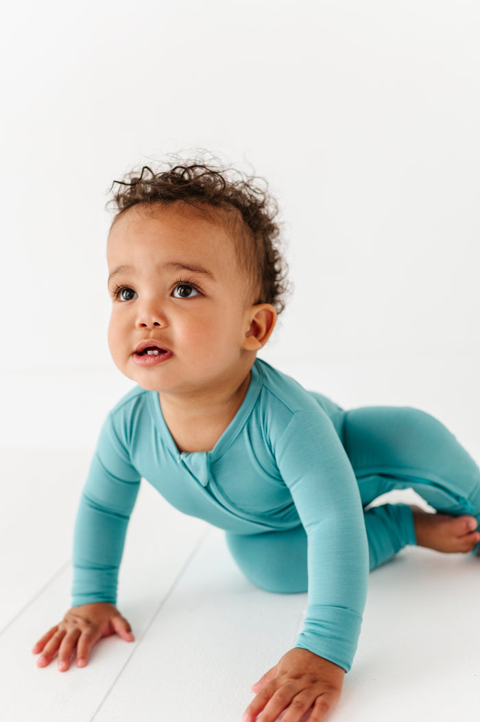 Baby in a slate blue bamboo zip romper on a white floor