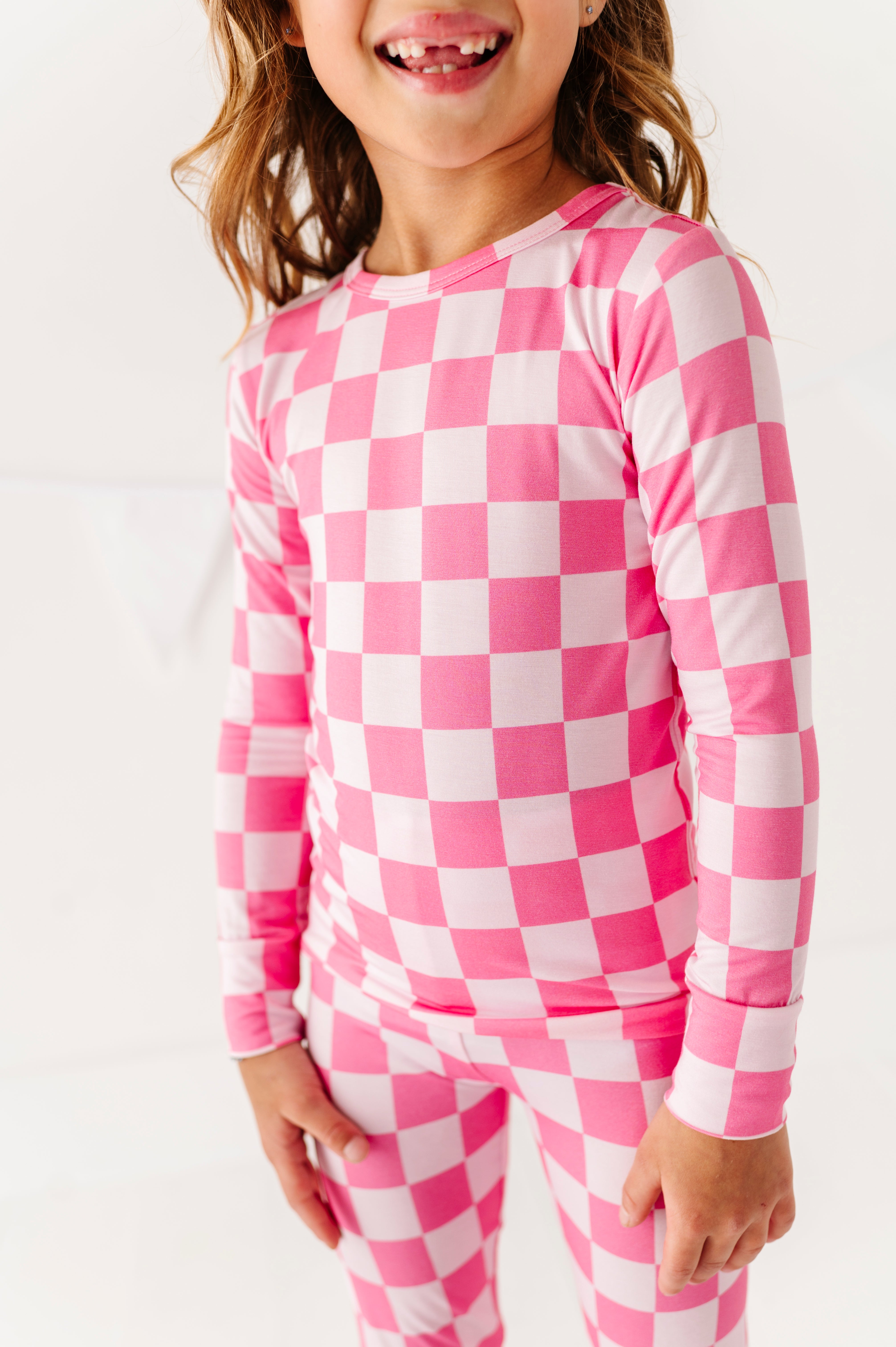 Child wearing pink and white checkered bamboo pajamas on a white background