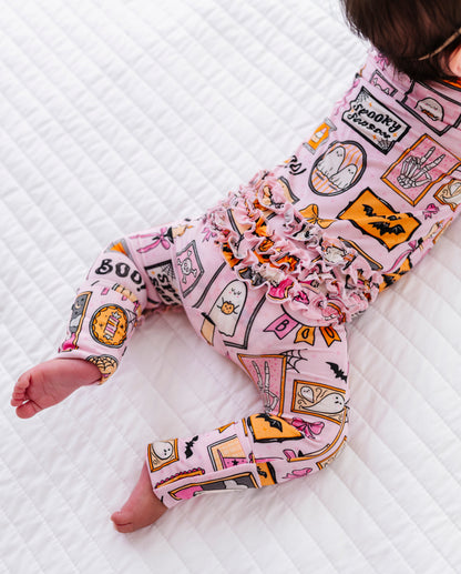 A baby wearing pink long-sleeve pajamas with a colorful Halloween-themed graphic print, lying on a white quilted mattress.