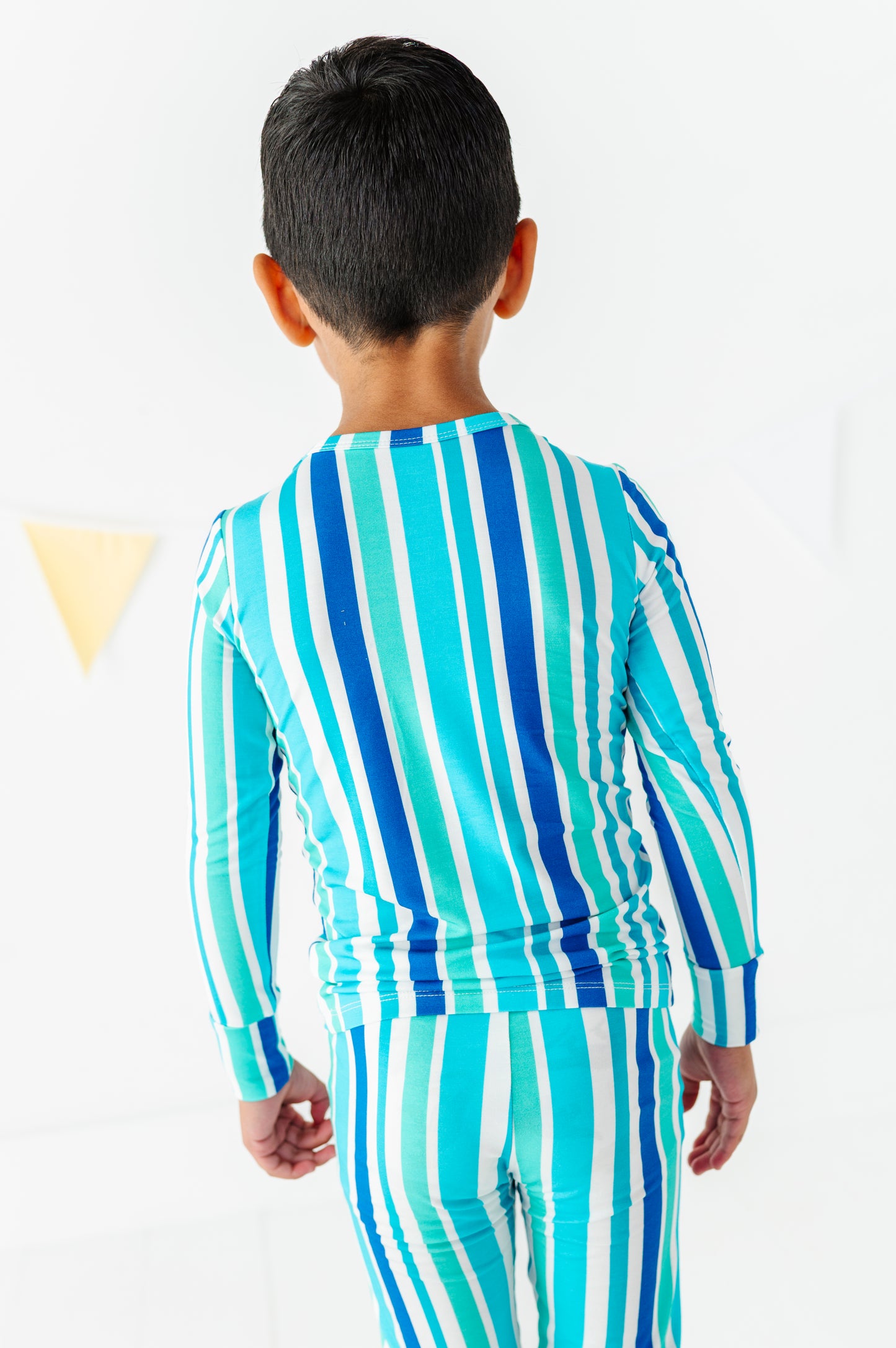 A child viewed from behind wearing a matching long-sleeve top and pants set with vertical stripes in turquoise, blue, and white.