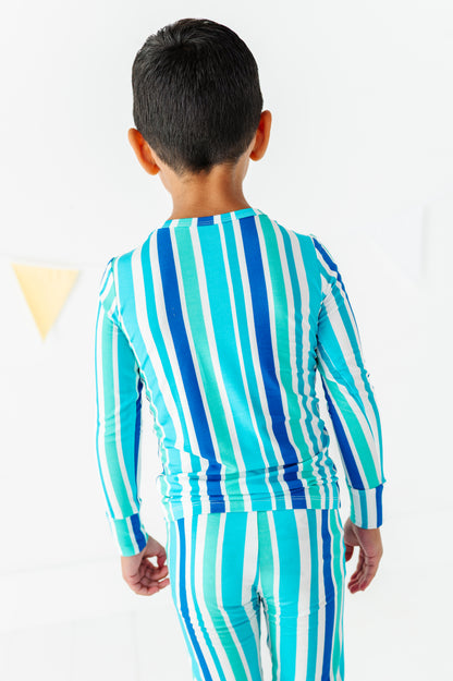 A child viewed from behind wearing a matching long-sleeve top and pants set with vertical stripes in turquoise, blue, and white.