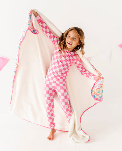 Child in pink checkered pajamas with a colorful blanket on a white background