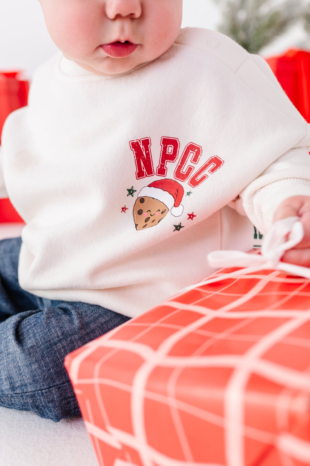 A close-up detail shot of the "NPCC" graphic on a baby's white crewneck 