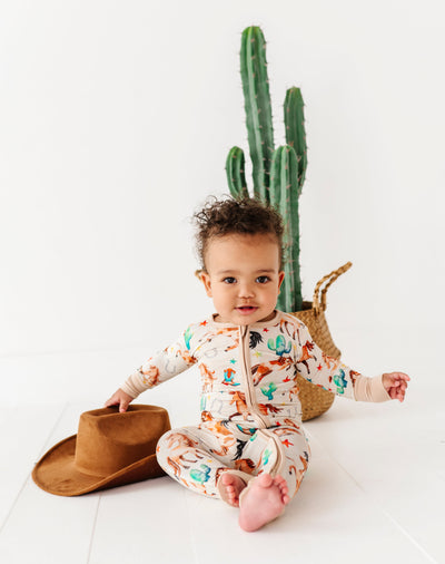 Baby in a patterned onesie with a cowboy hat and cactus in the background