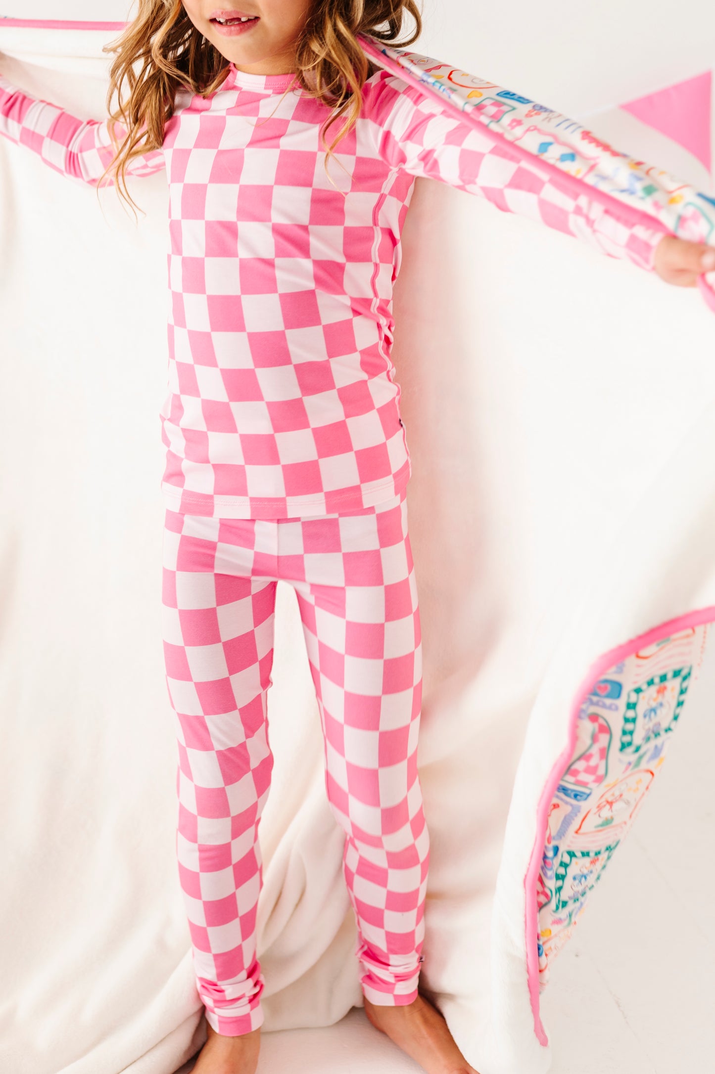Child wearing pink and white checkered bamboo pajamas with a colorful towel.