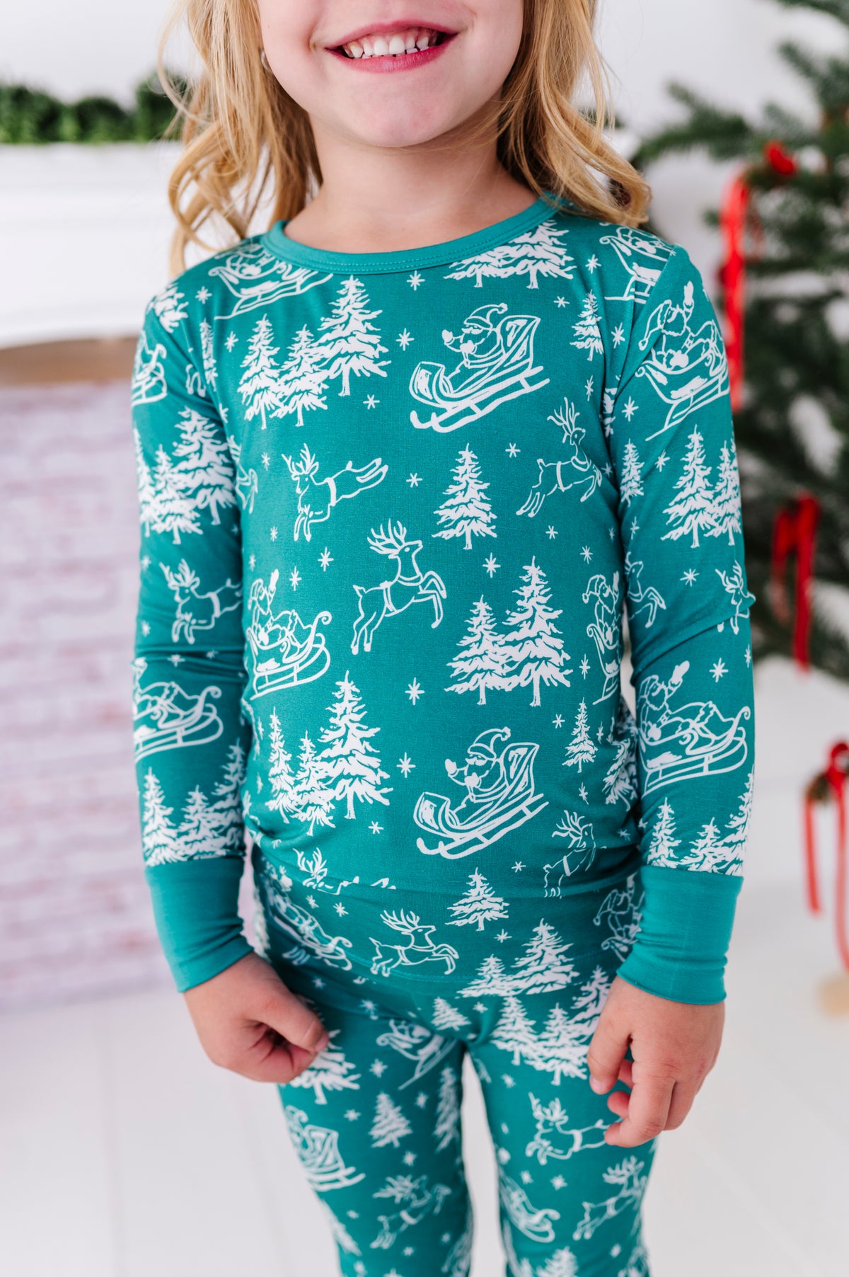 A close-up detail shot of a little girl wearing a bamboo two-piece pajama set featuring vintage sleighs, reindeer, and Santa. 
