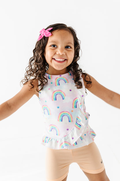 Young girl wearing a bamboo cotton peplum top with watercolor rainbow pattern and peach bamboo biker shorts on a white background