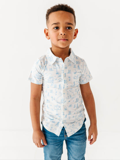 Young boy wearing a white shirt with blue patterns and blue jeans on a white background