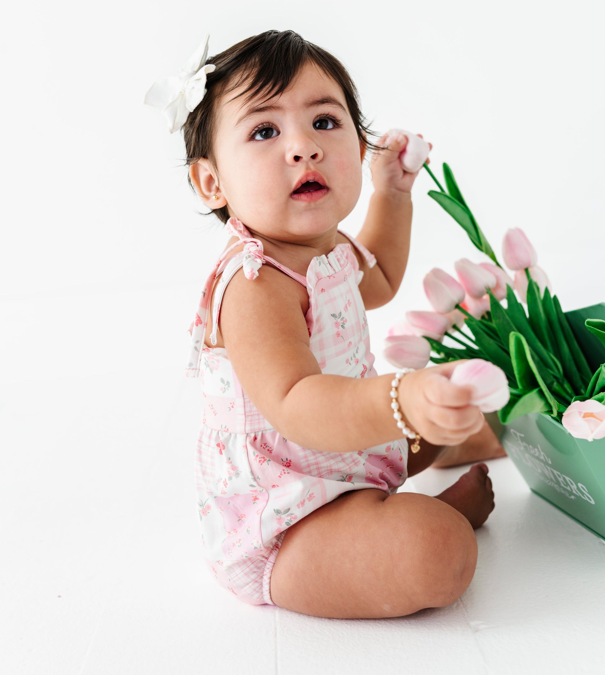 Baby in a floral bamboo bubble romper holding pink tulips on a white background