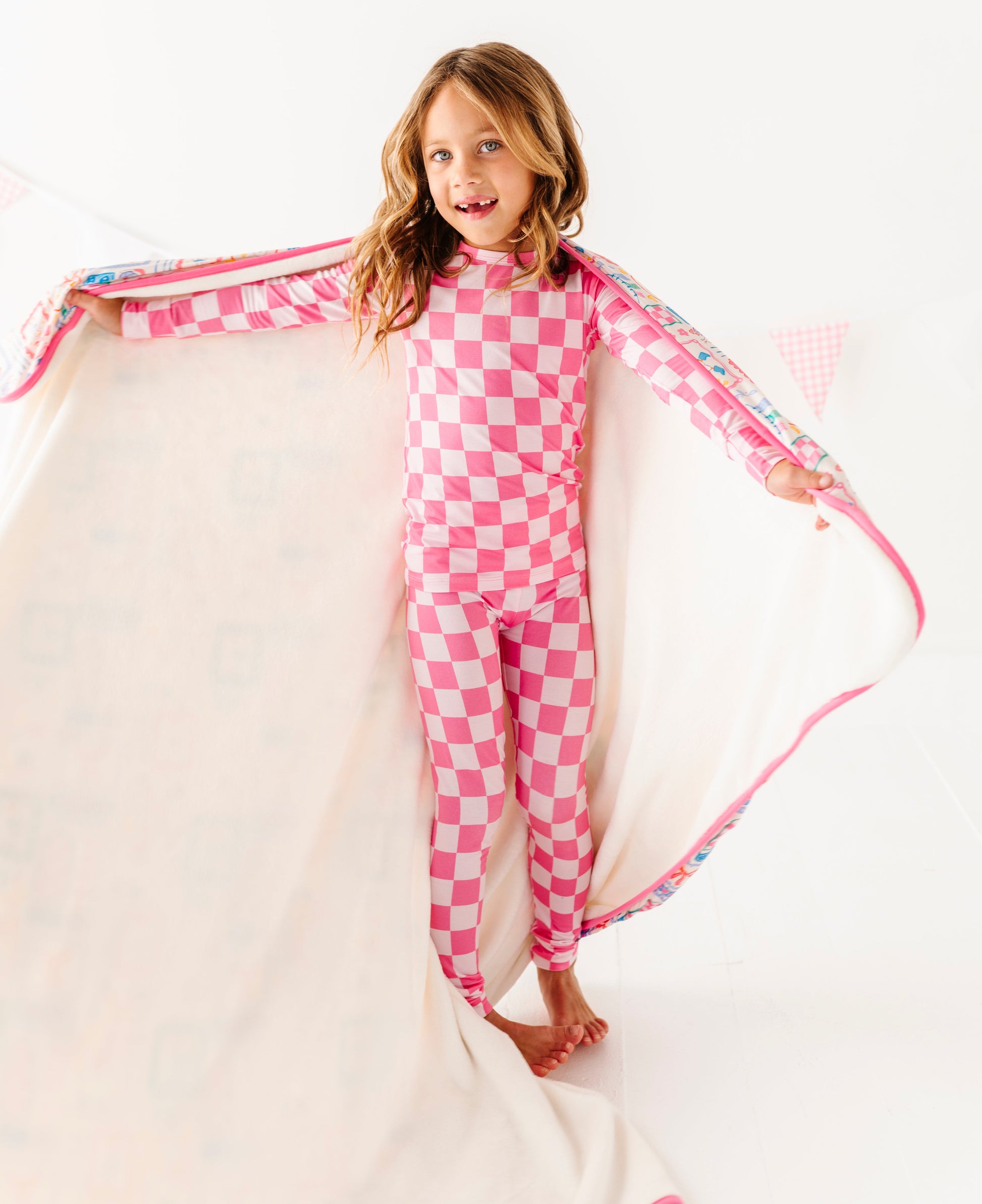 Child wearing pink checkered bamboo pajamas with a plush blanket wrapped around her