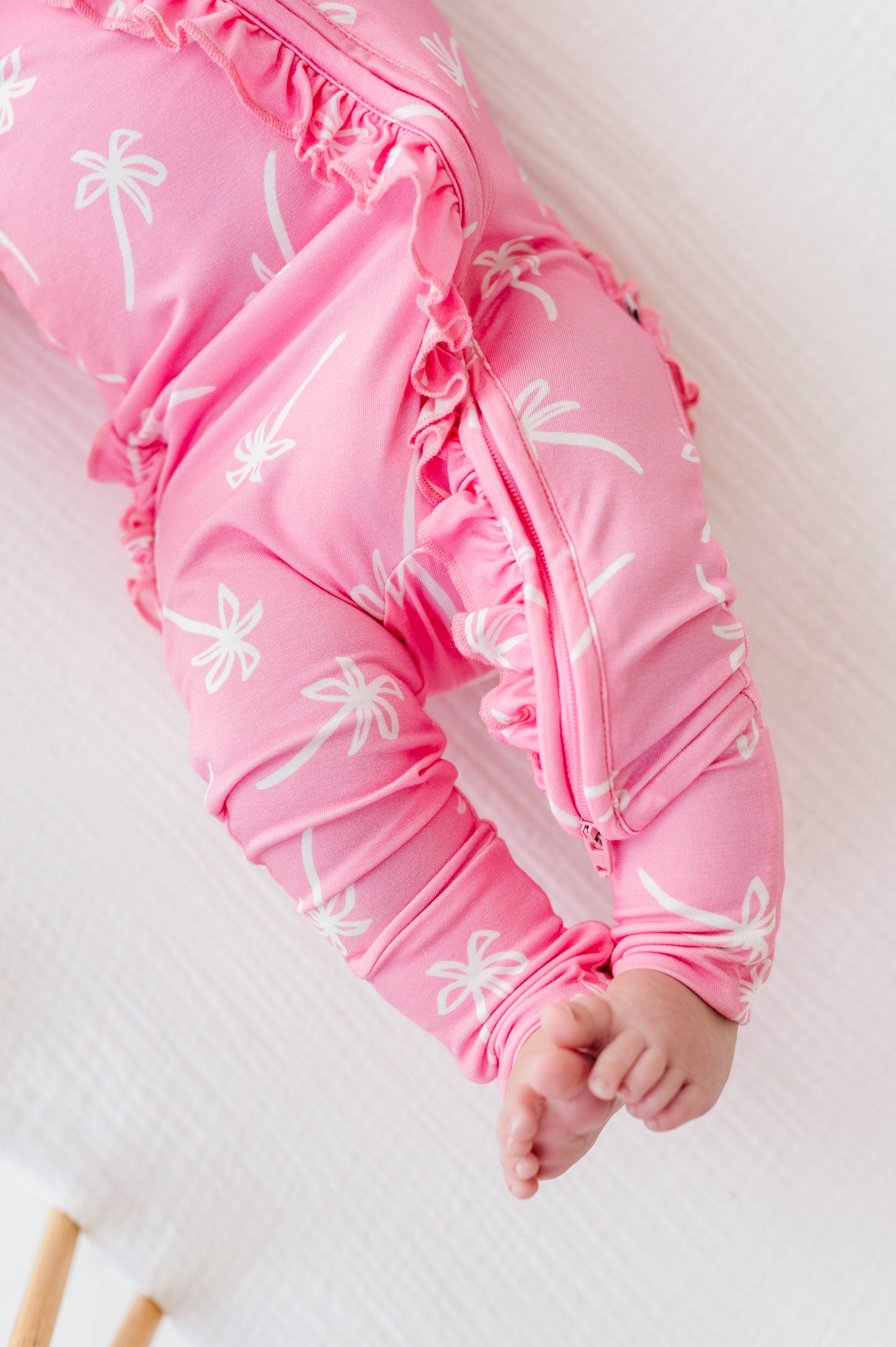 Pink baby romper with white palm tree patterns on a light background