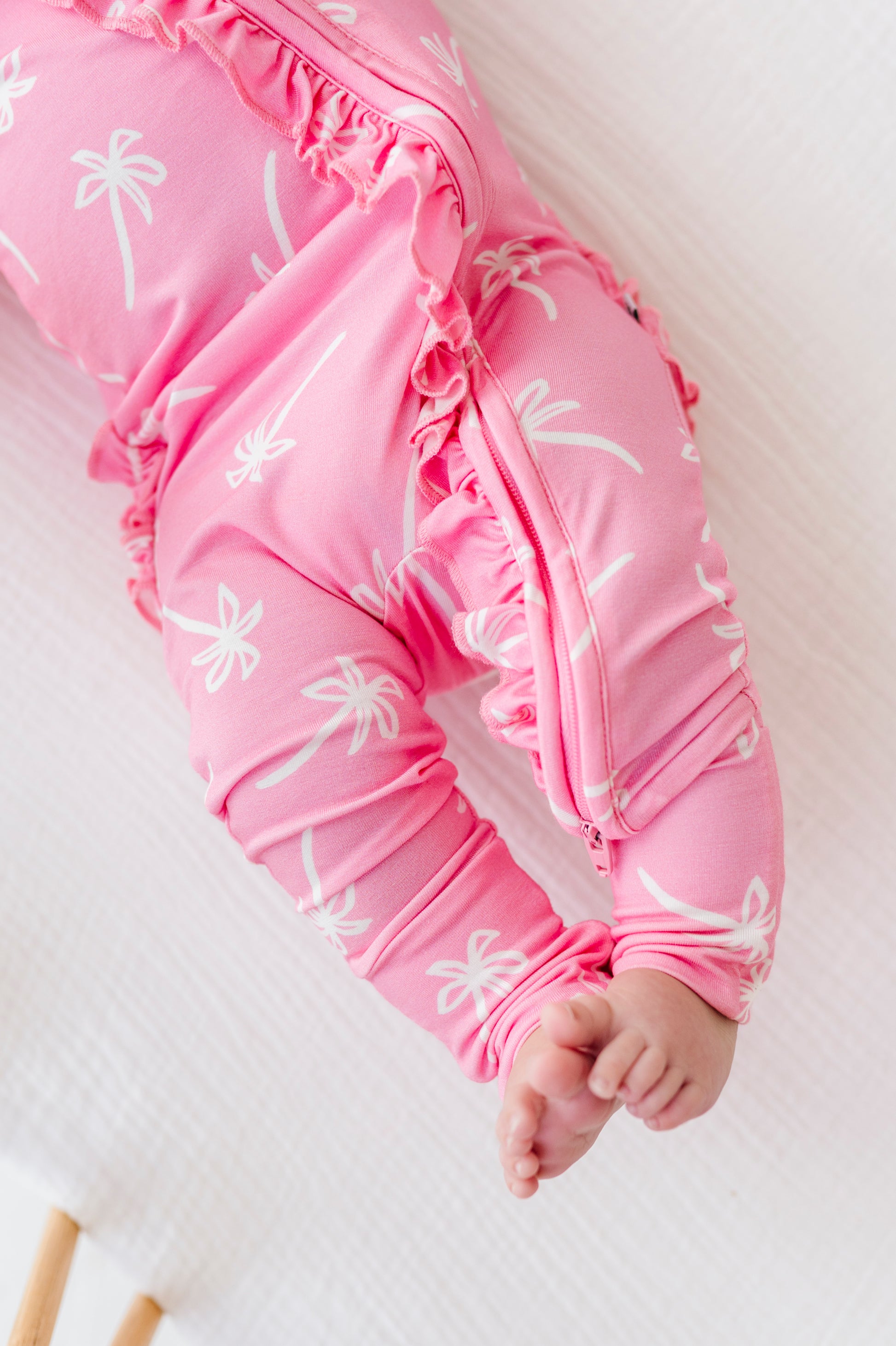 Pink baby romper with white palm tree patterns on a light background