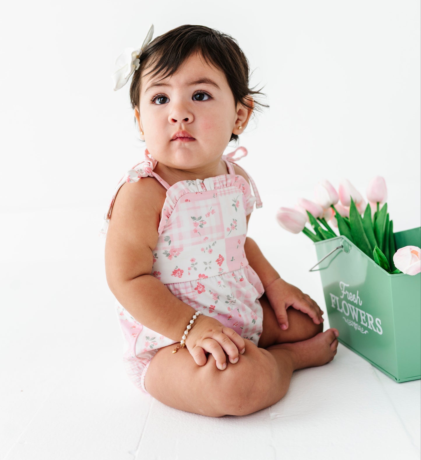 Child in a floral bamboo romper sitting next to a box of flowers on a white background