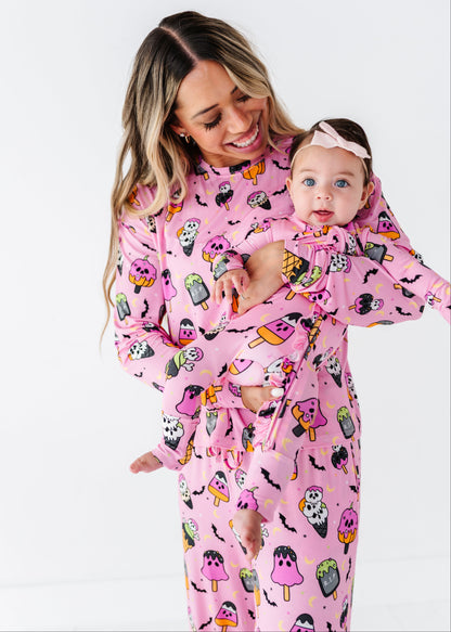 A woman and a baby wearing matching pink Halloween-themed pajamas with a ghostly ice cream cone pattern, photographed against a clean white studio background.