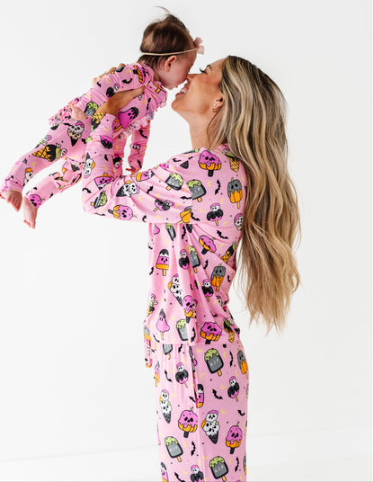 A woman and a child wearing matching pink pajamas with a colorful cartoon cupcake pattern, posed against a clean white studio background.