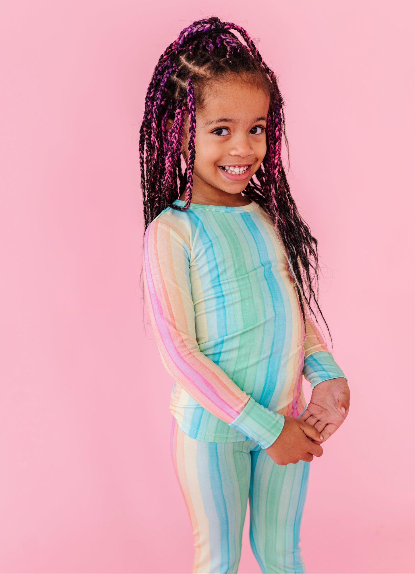 Child wearing a pastel striped bamboo pajama set on a pink background