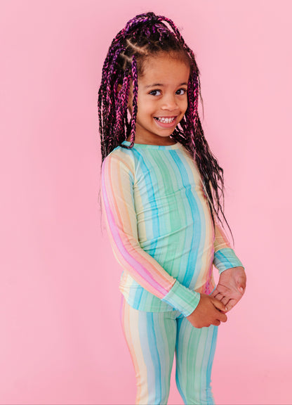 Child wearing a pastel striped bamboo pajama set on a pink background