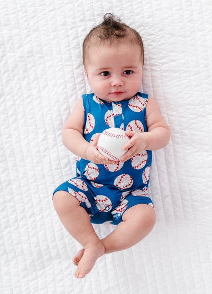 Baby wearing a blue bamboo outfit with baseball pattern, holding a small baseball on a white textured surface.