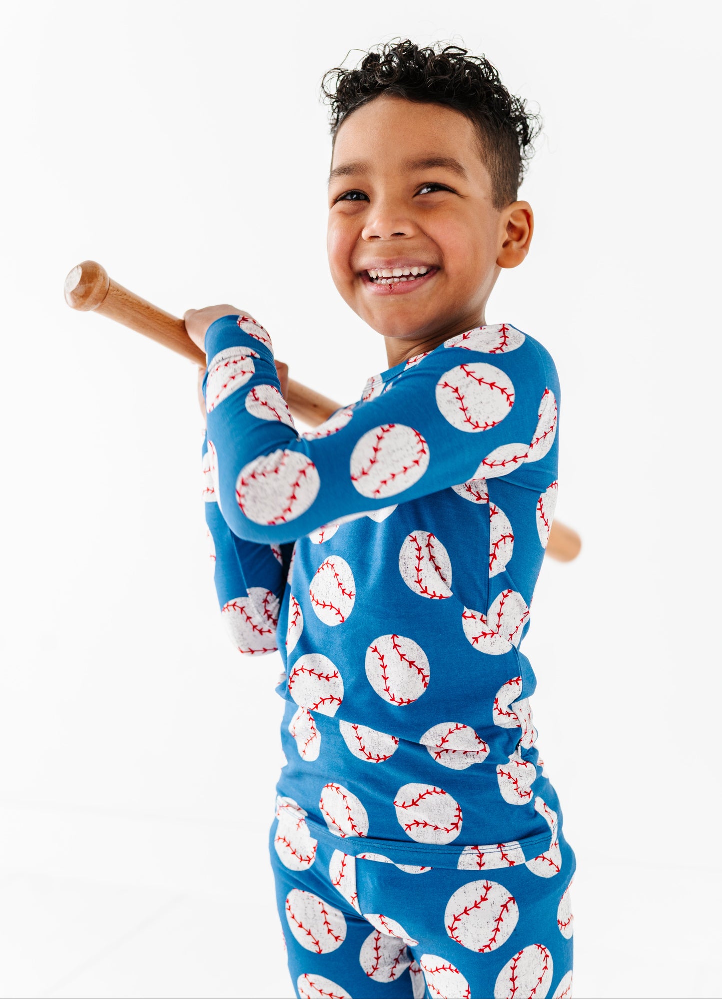 Child wearing a blue bamboo pajama set with baseball pattern, holding a wooden bat.