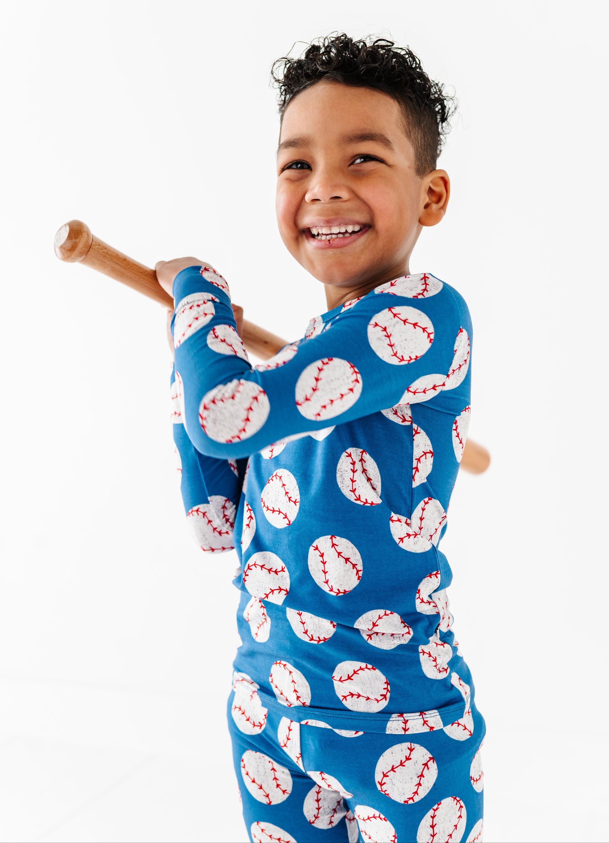 Child wearing a blue bamboo pajama set with baseball pattern, holding a wooden bat.