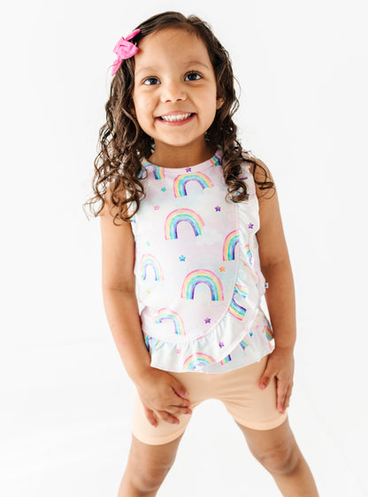 Young girl wearing a sleeveless bamboo cotton top with rainbow patterns and peach bamboo shorts on a white background