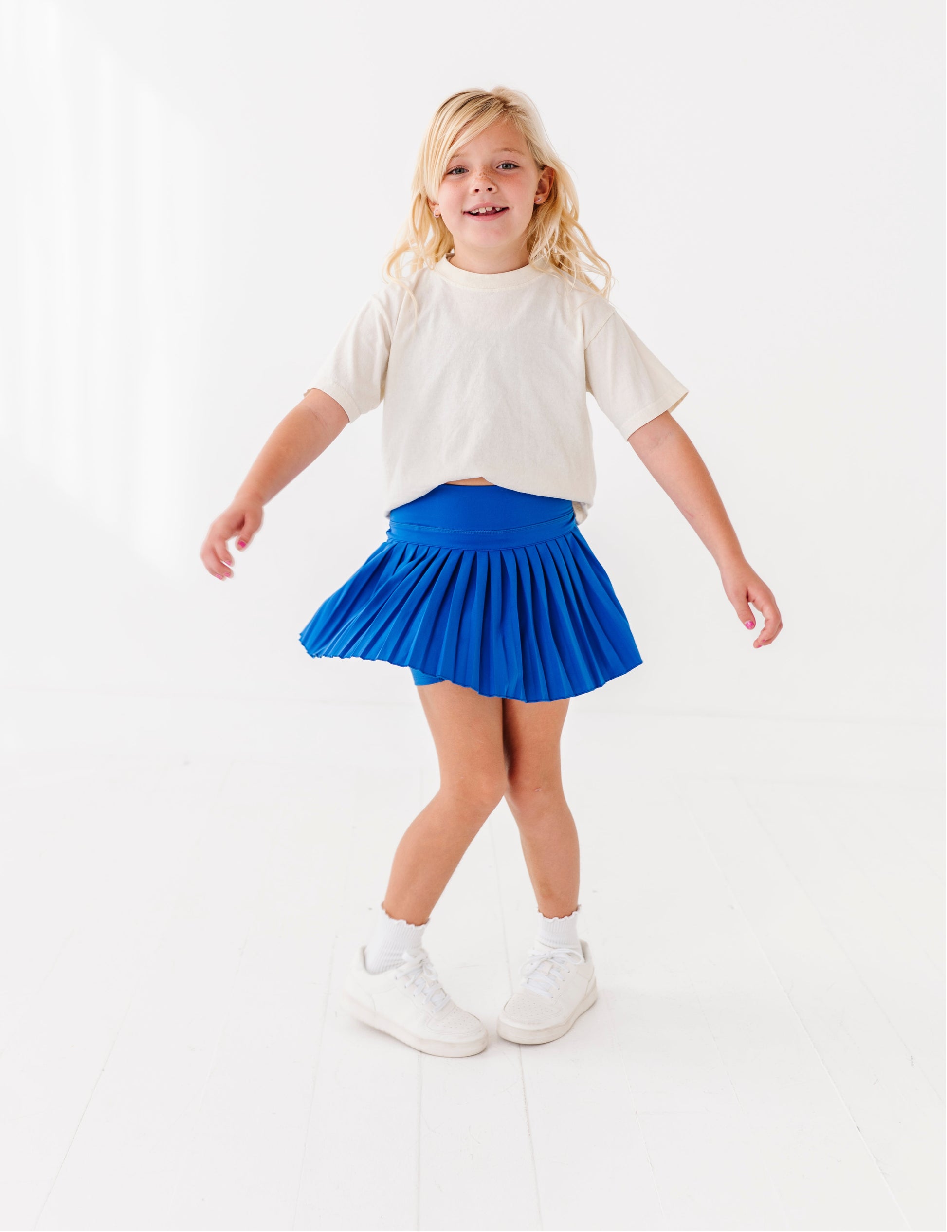 Young girl wearing a white t-shirt and blue activewear skort on a white background
