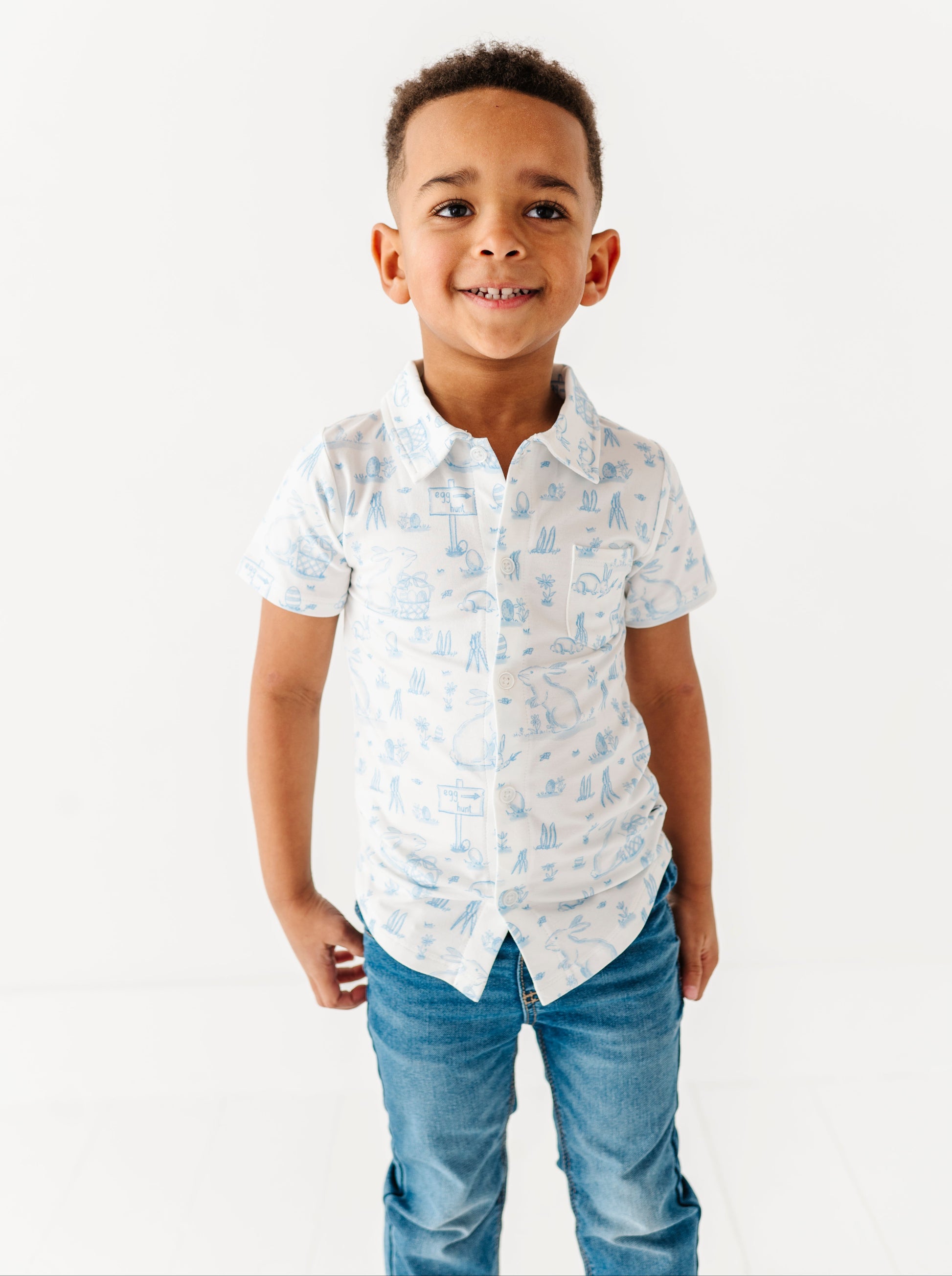 Young boy wearing a white shirt with blue patterns and blue jeans on a white background