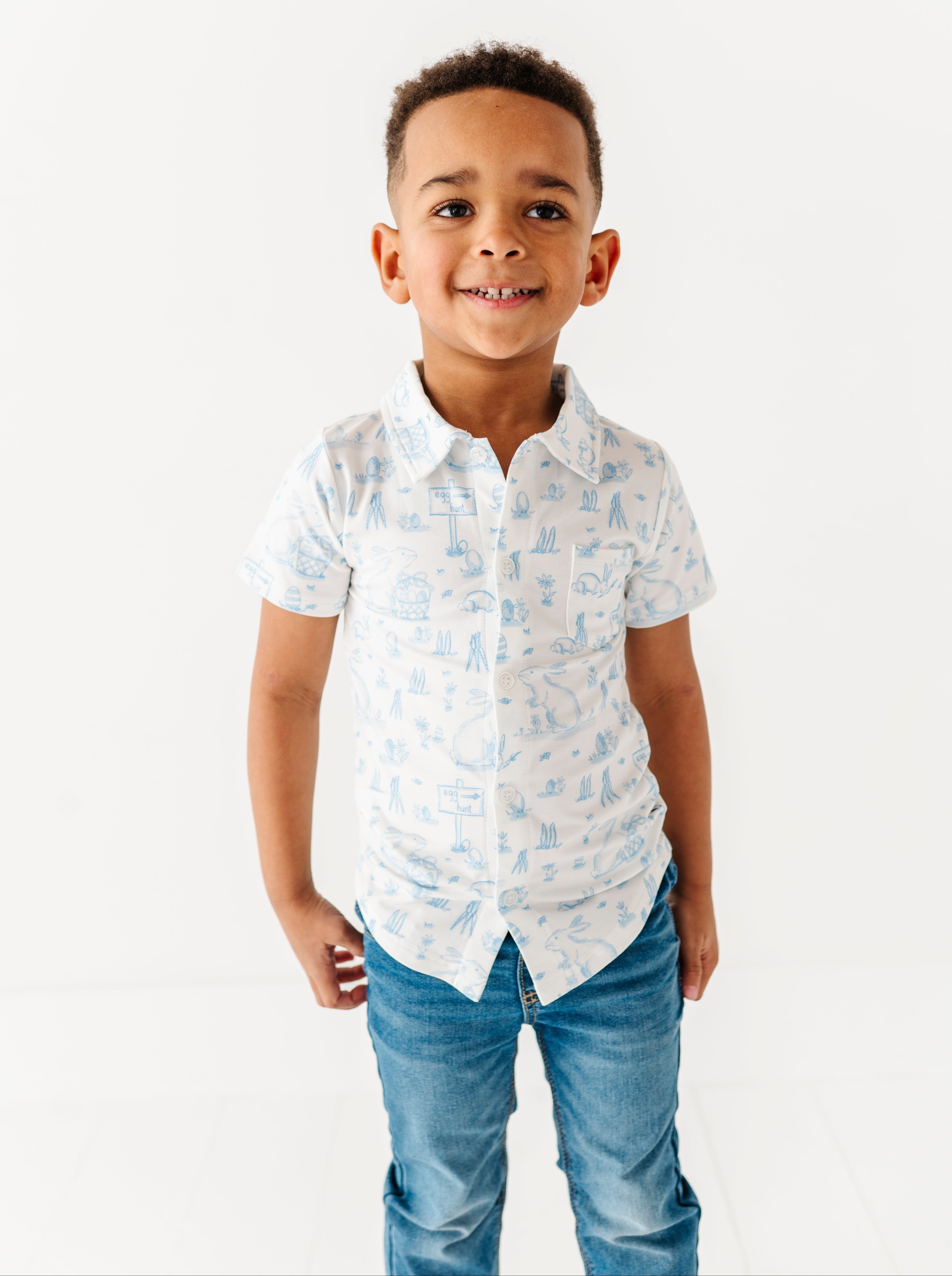 Young boy wearing a white shirt with blue patterns and blue jeans on a white background