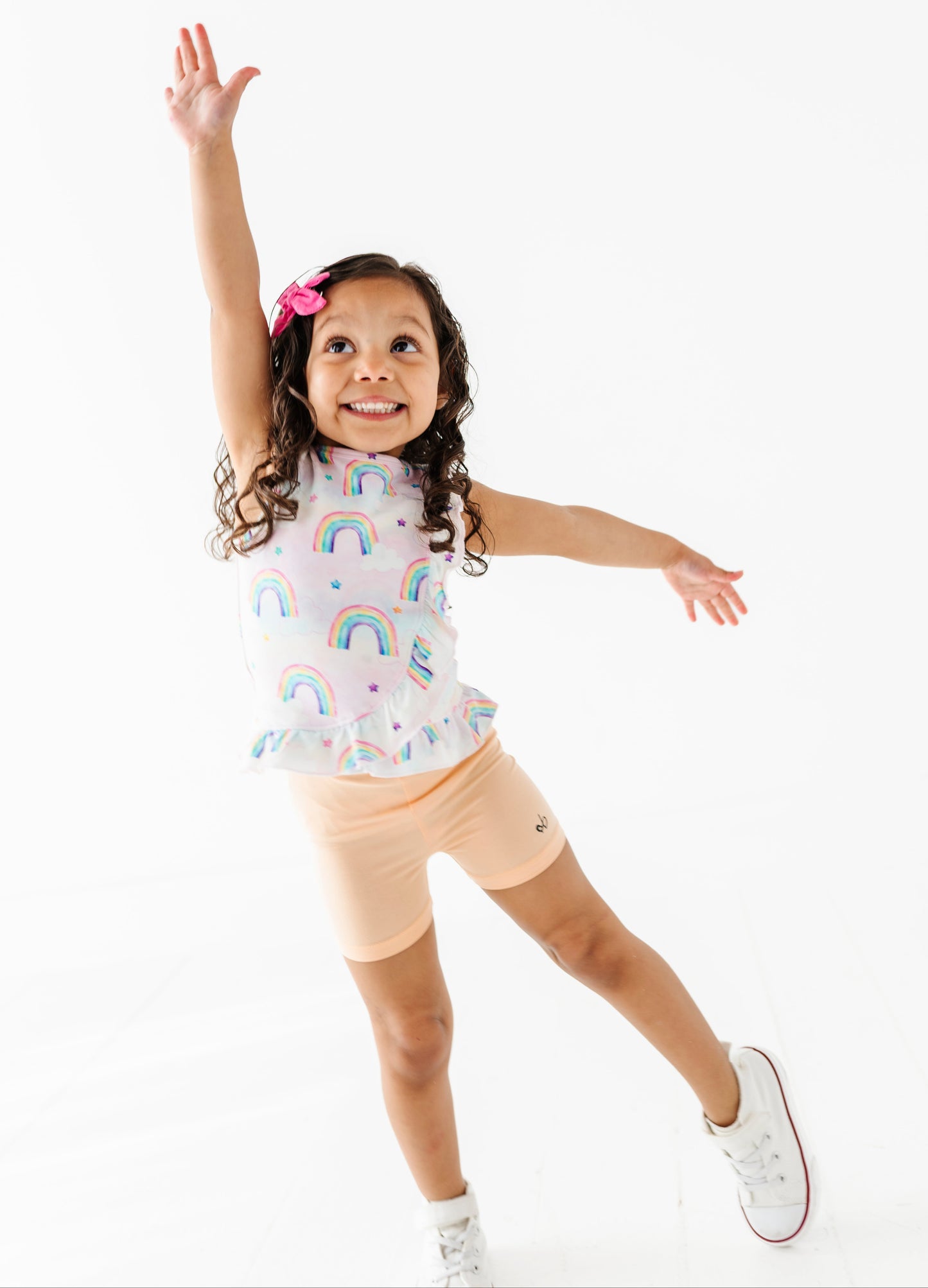 Child wearing a bamboo cotton peplum top with rainbow watercolor patterns and peach bamboo biker shorts on a white background