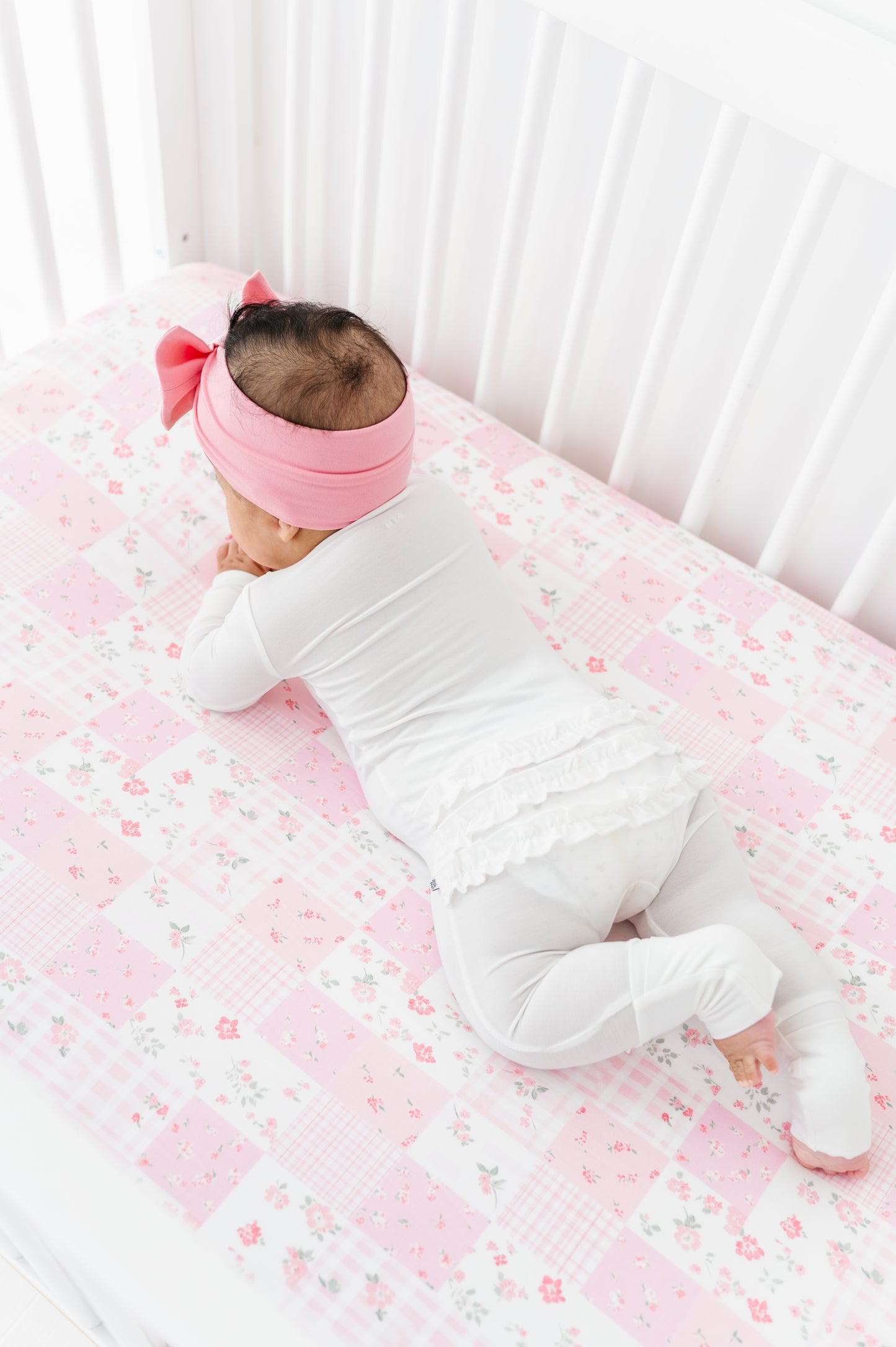 Baby lying on a crib with pink floral bamboo bedding and a pink headband.