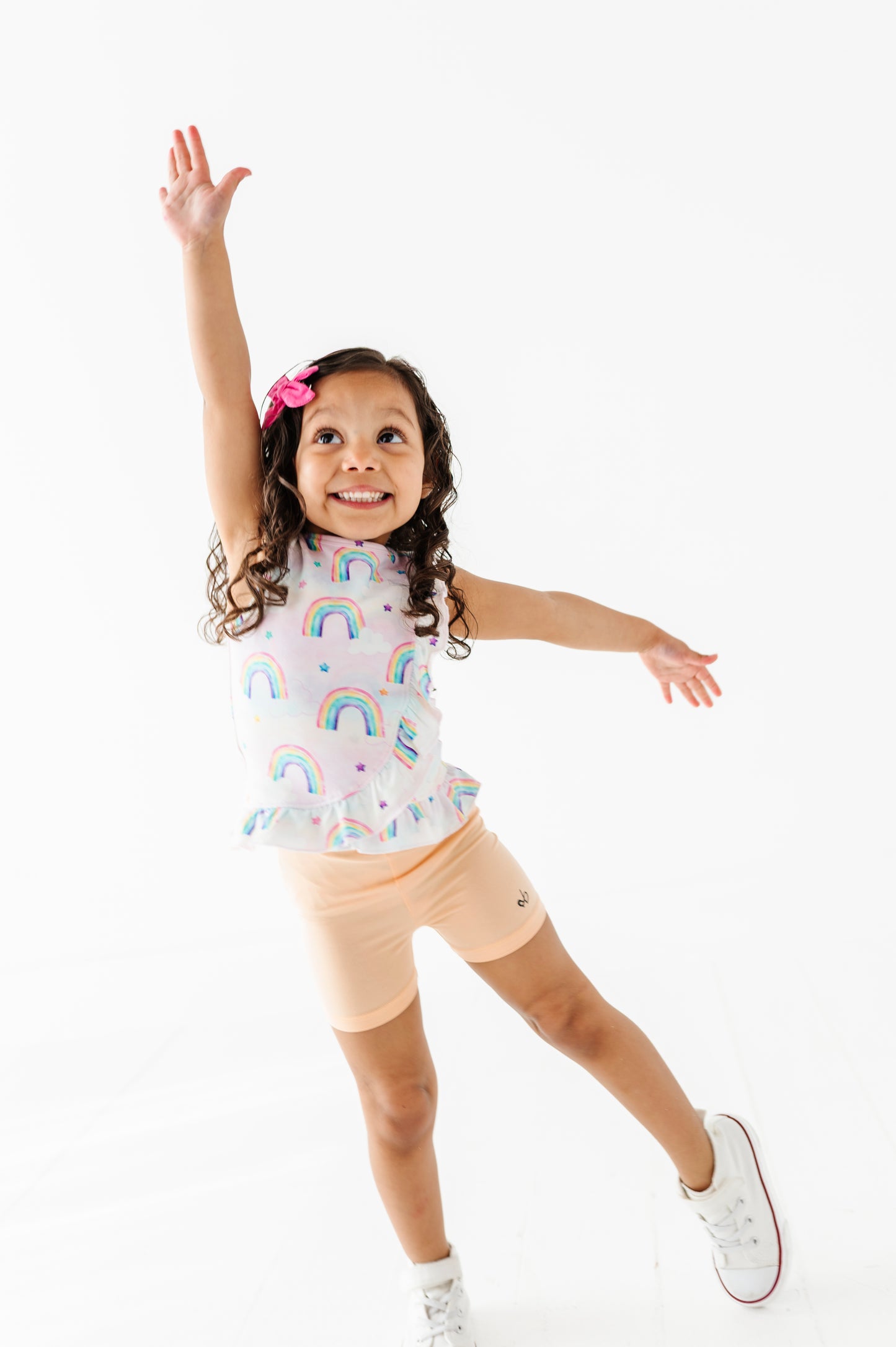 Child wearing a bamboo cotton peplum top with watercolor rainbow patterns and peach colored bamboo biker shorts on a white background