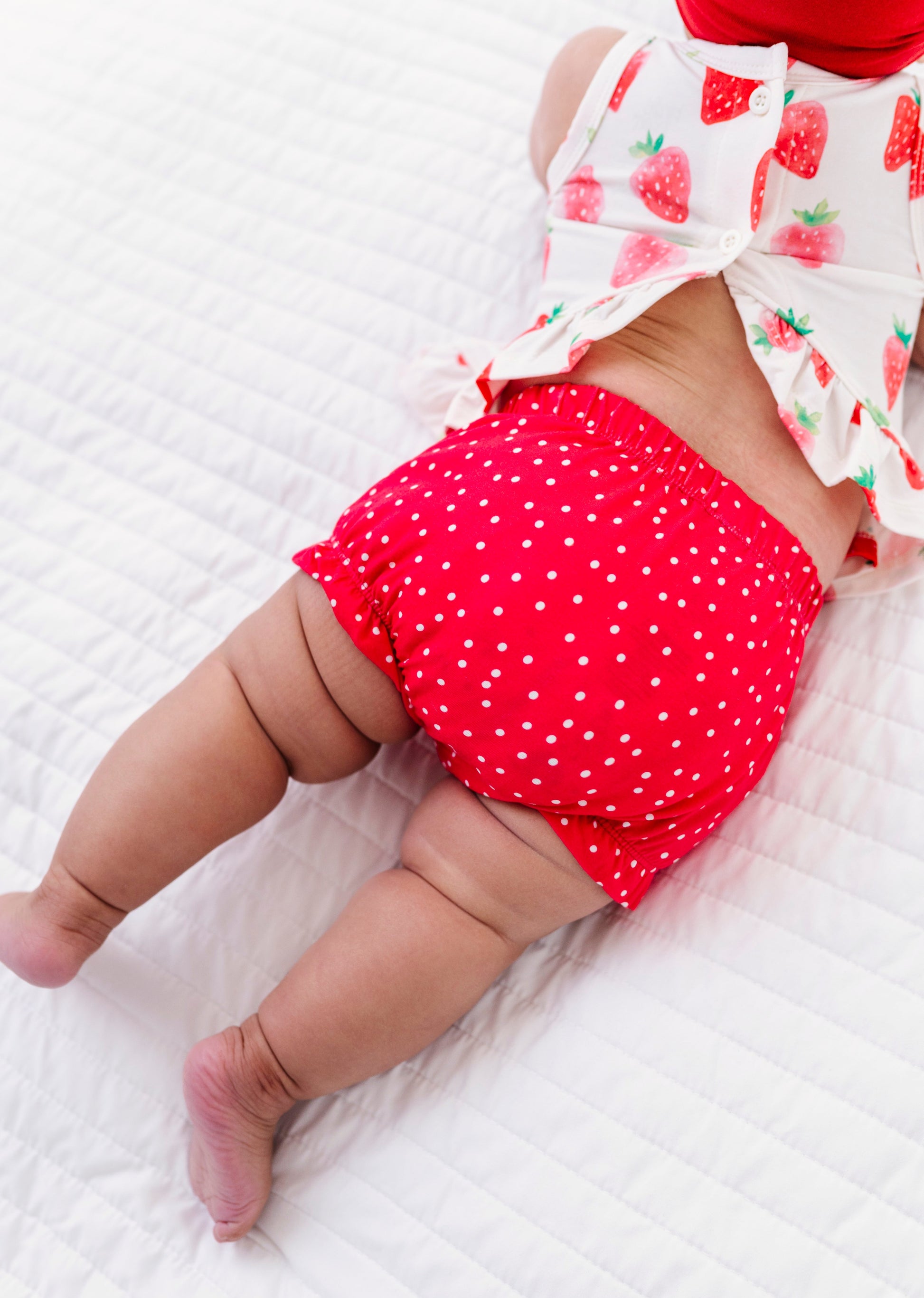 Baby wearing a red polka dot bloomer on a white textured surface