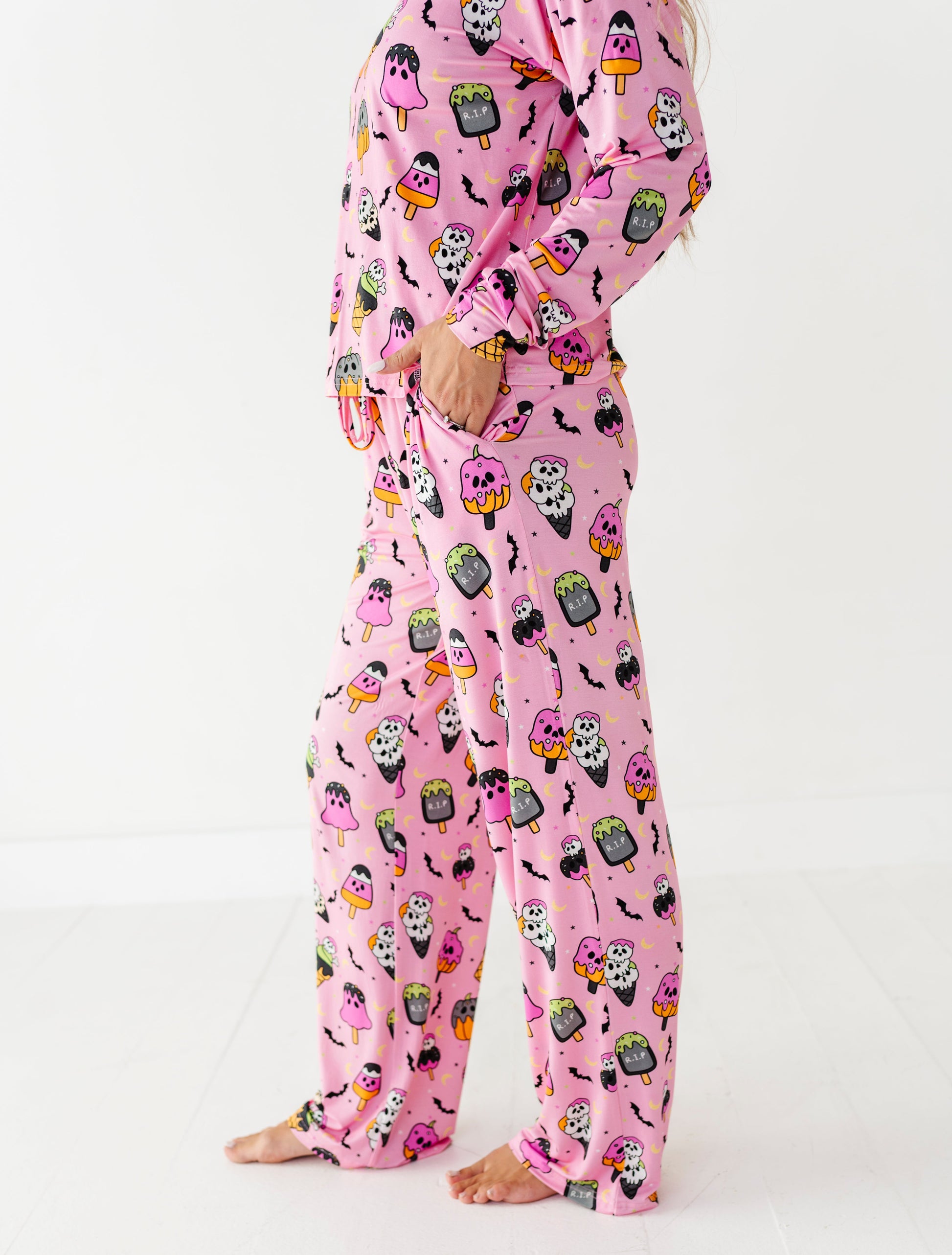 A person wearing a pink long-sleeve pajama set with a cartoon monster print, standing barefoot against a clean white studio background.