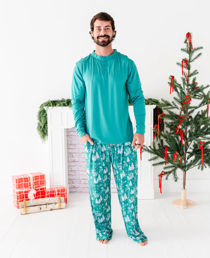 A dad wearing bamboo pajama bottoms with a bamboo henley top. The henley is a solid seafoam green, while the pants feature a vintage print including Santa, his reindeer, and pine trees. 