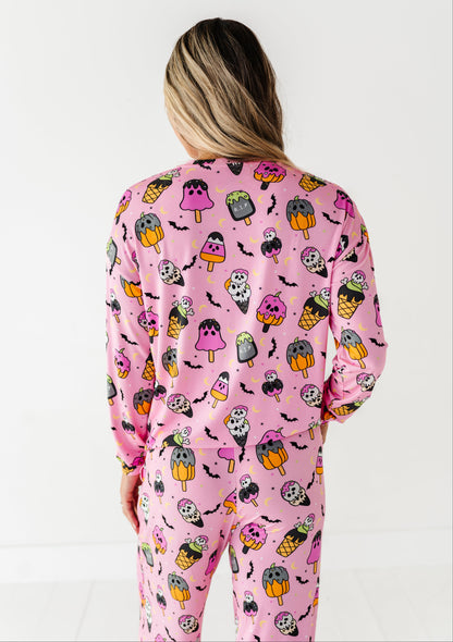 A woman viewed from behind wearing a pink long-sleeve pajama set with a colorful cartoon ice cream cone and ghost pattern, against a plain white background.