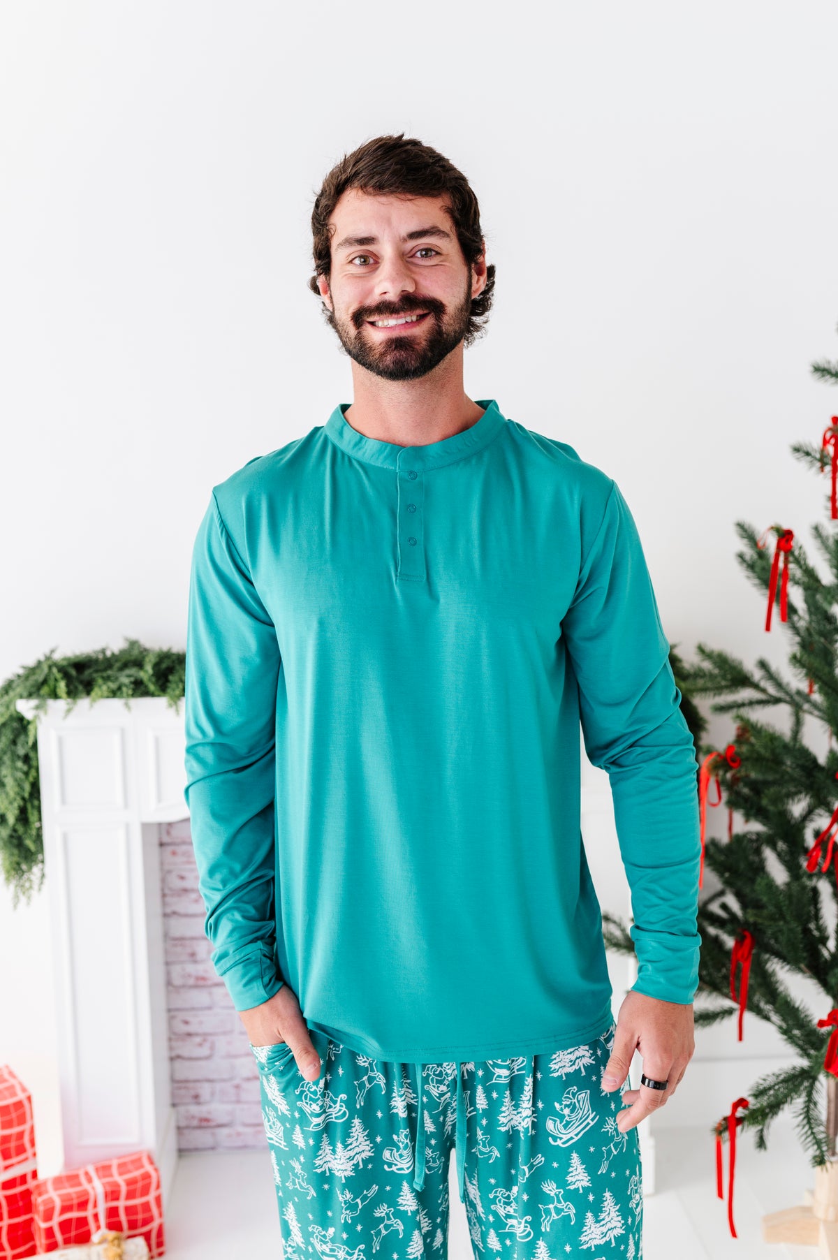 A photo of a smiling dad wearing a bamboo pajama set, including a seafoam green henley top and vintage sleigh bamboo pajama bottoms 