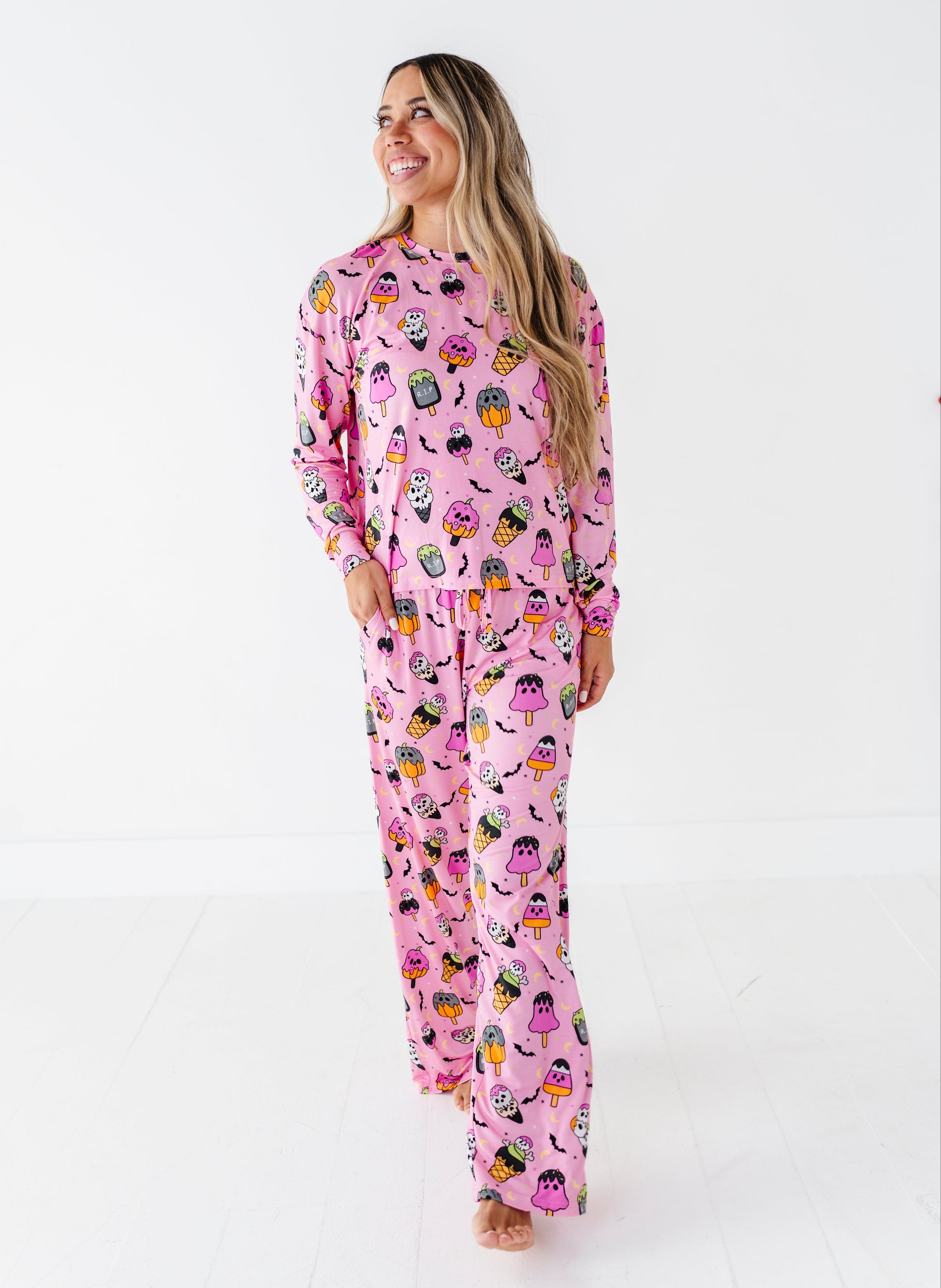 A woman modeling a pink long-sleeve pajama set with a colorful cartoon character print, standing against a plain white studio background.