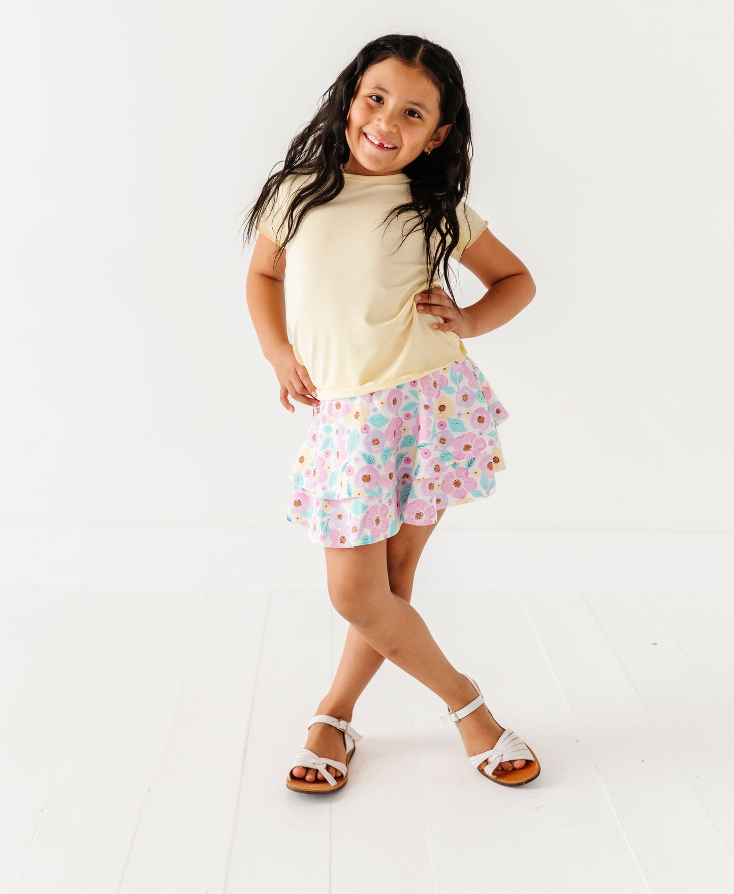 Young girl wearing a light-colored buttercream top and floral bamboo skort on a white background