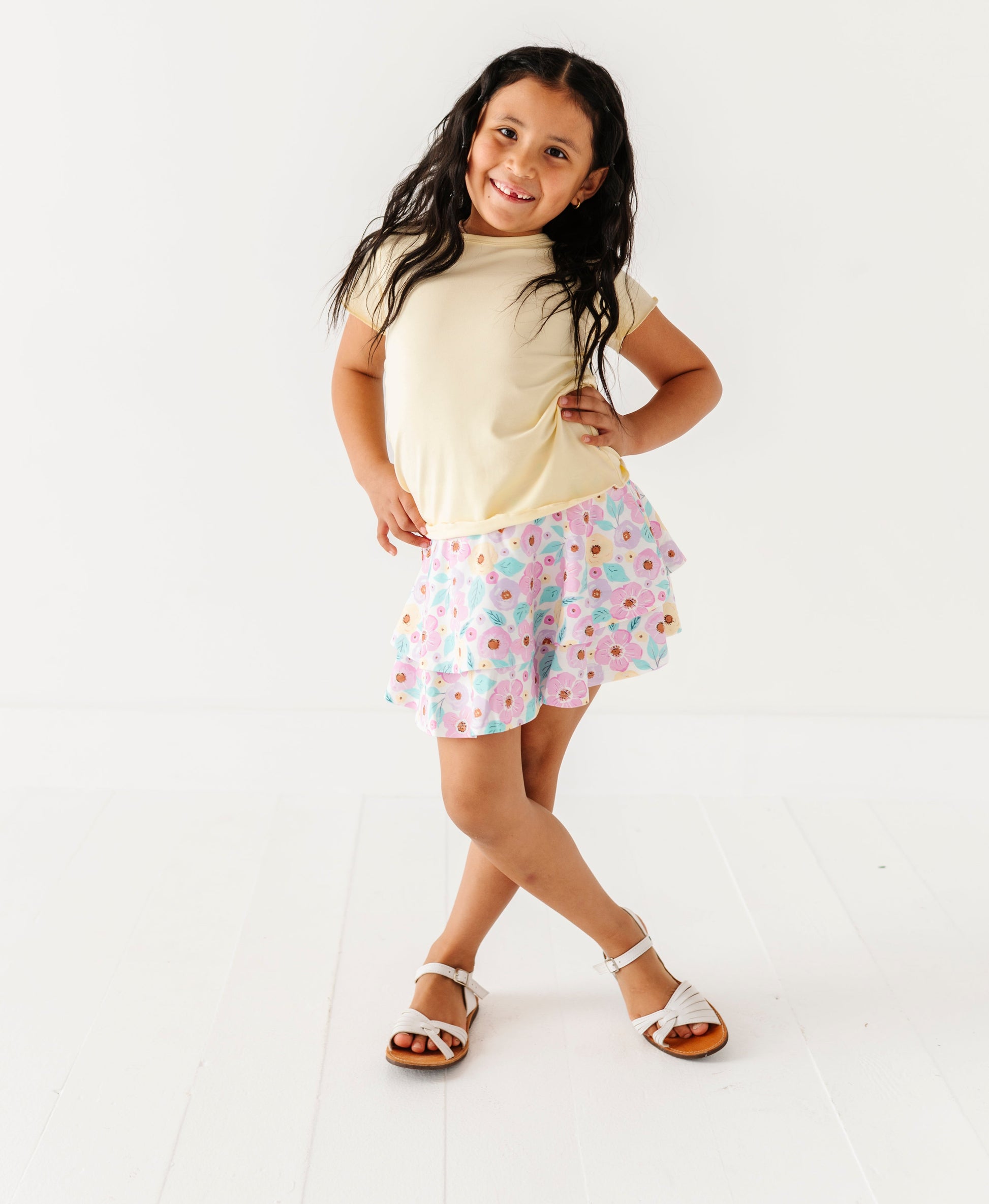 Young girl wearing a light-colored buttercream top and floral bamboo skort on a white background