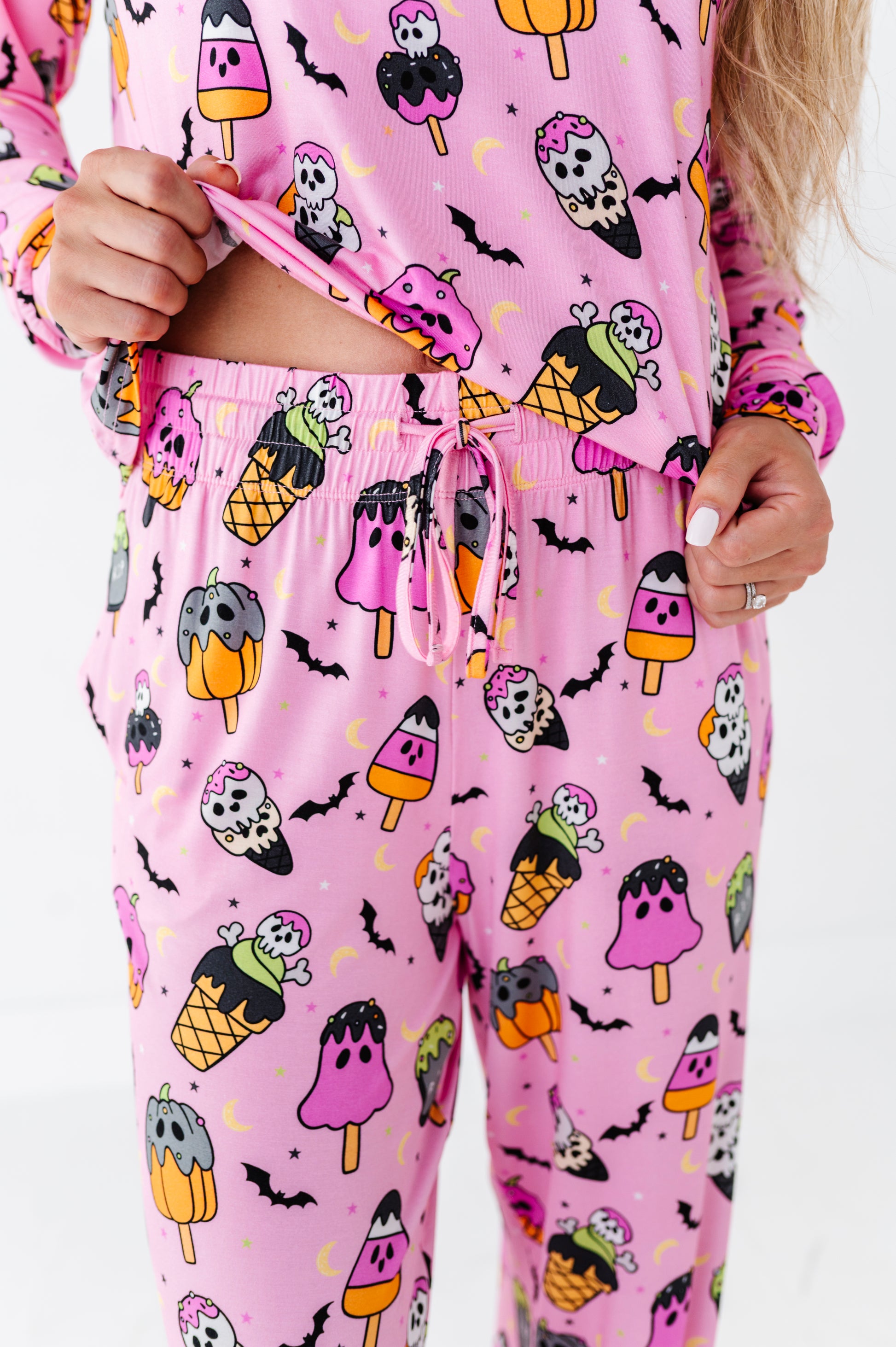 A person wearing a pink long-sleeve pajama set with an all-over Halloween ice cream print, including ghosts, bats, and ice cream cones, photographed against a plain white background.