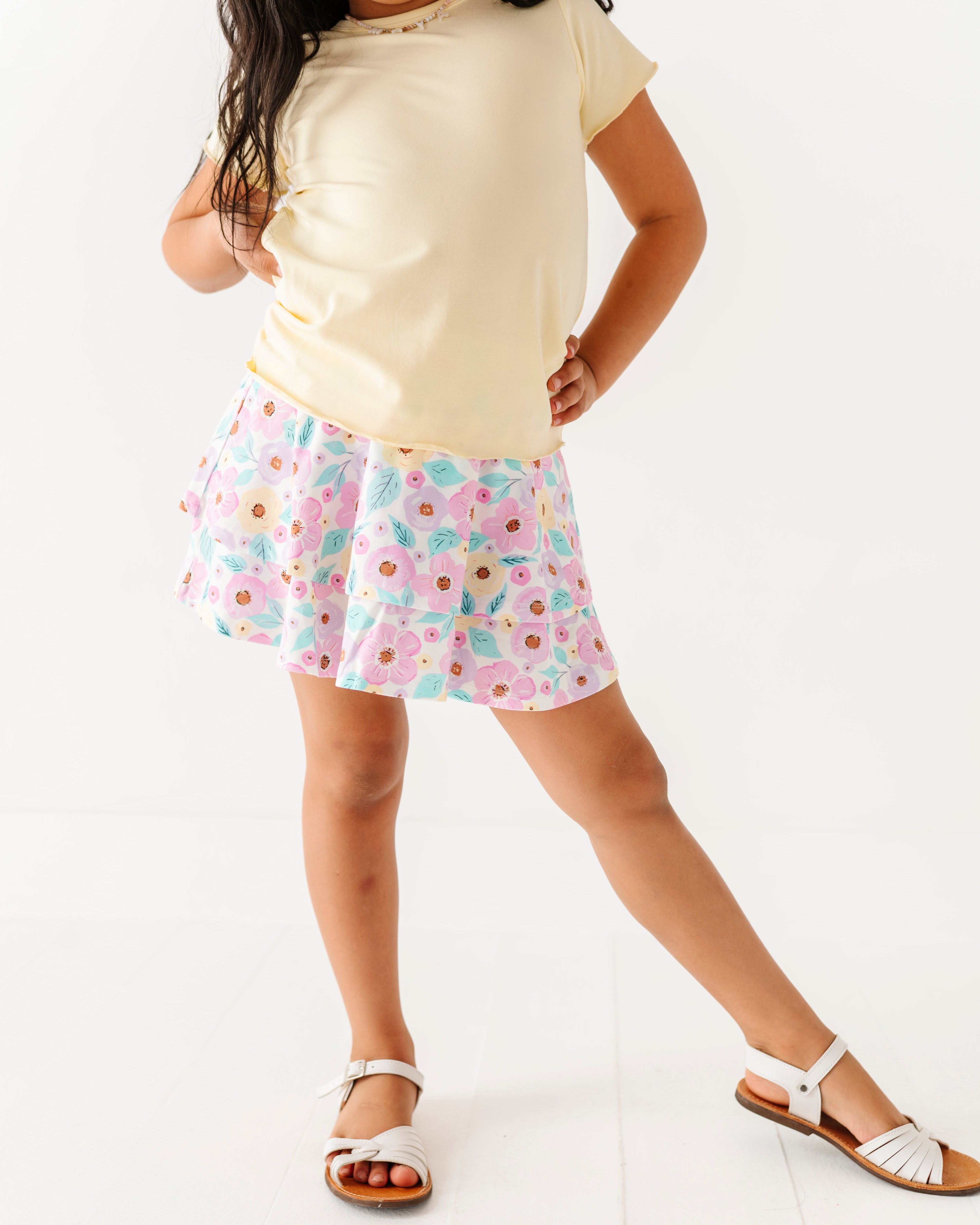 Child wearing a buttercream top and a floral skort on a white background