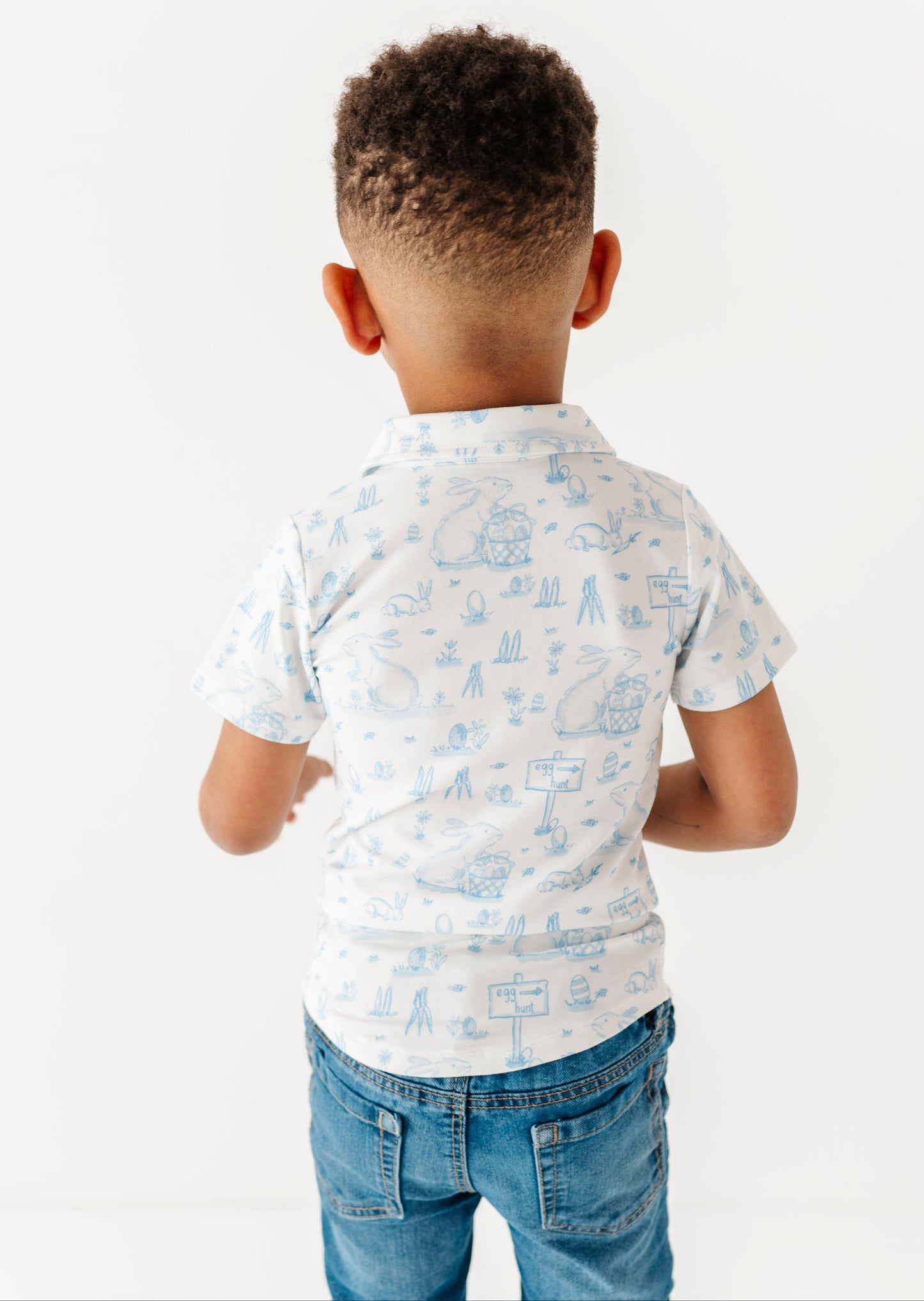 Child wearing a white shirt with blue patterns and blue jeans on a white background