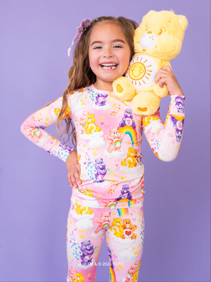 Child wearing a colorful pajama set with cartoon characters, holding a yellow teddy bear against a purple background.