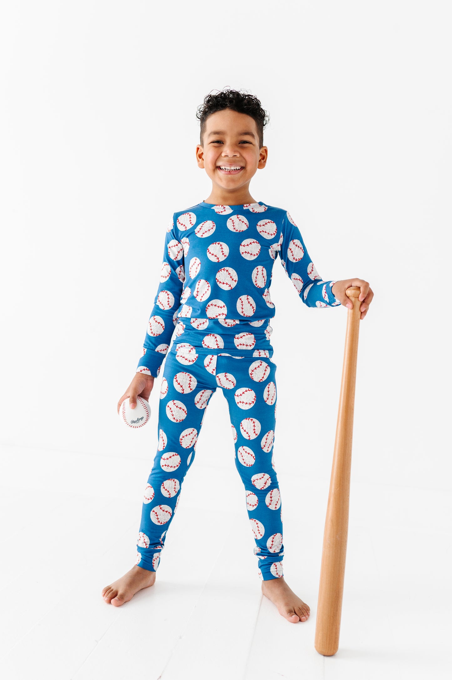 Child wearing a blue bamboo pajama set with baseball pattern, holding a wooden bat on a white background