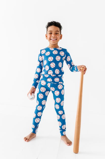 Child wearing a blue bamboo pajama set with baseball pattern, holding a wooden bat on a white background