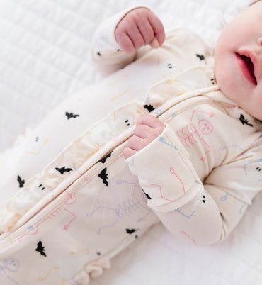 Baby in a cream outfit with a halloween pattern on a white background