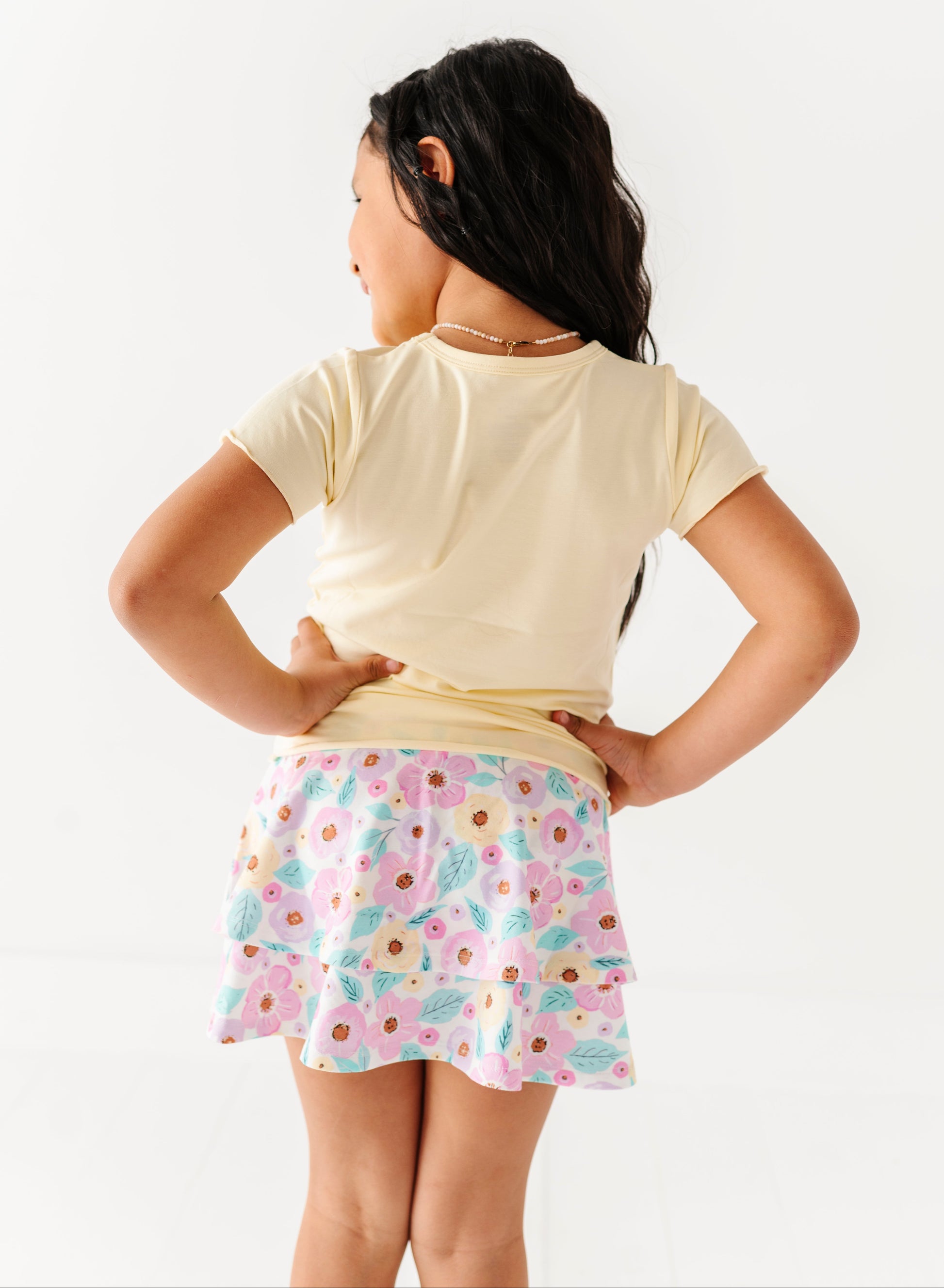 Child wearing a light-colored buttercream bamboo shirt and floral skort on a white background