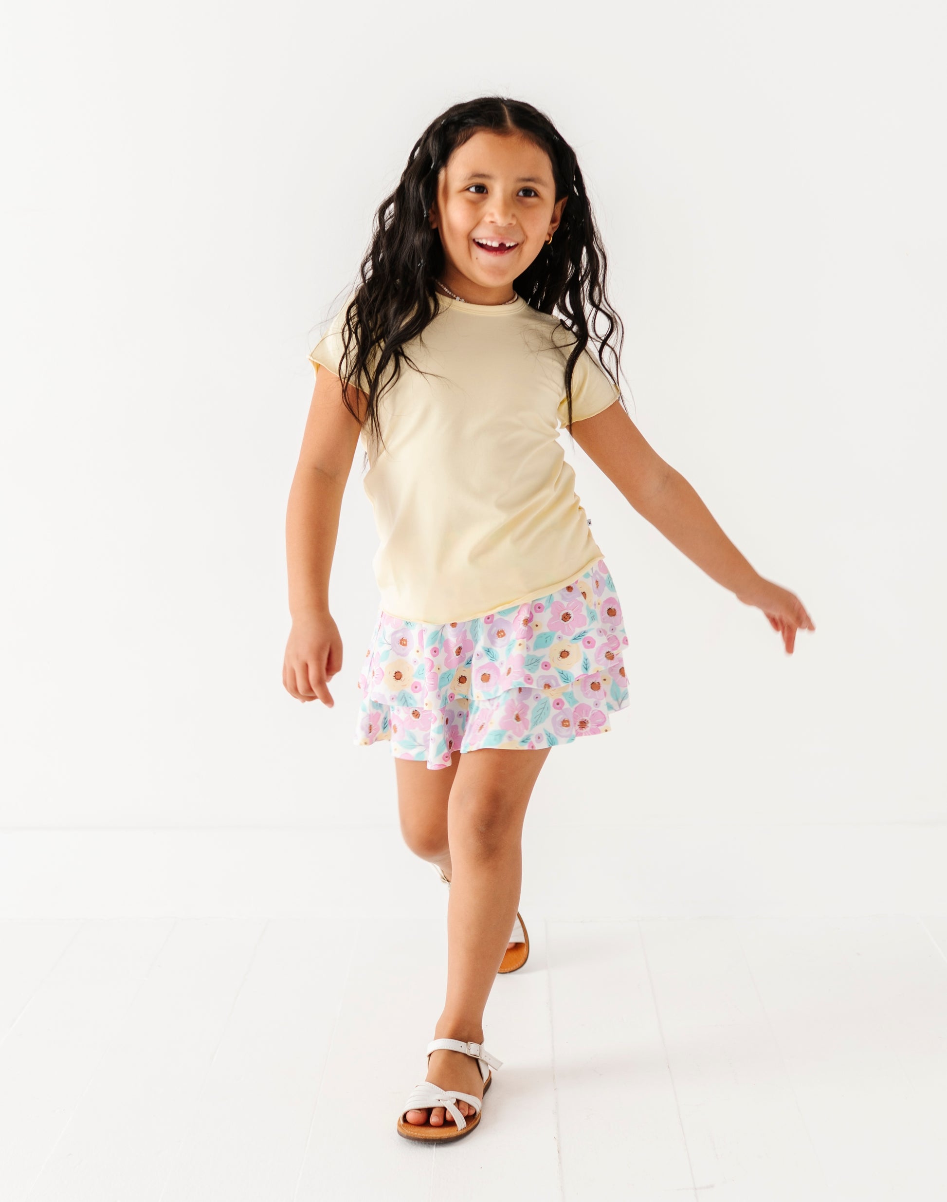 Young girl wearing a yellow shirt and floral skort on a white background