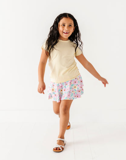 Young girl wearing a yellow shirt and floral skort on a white background